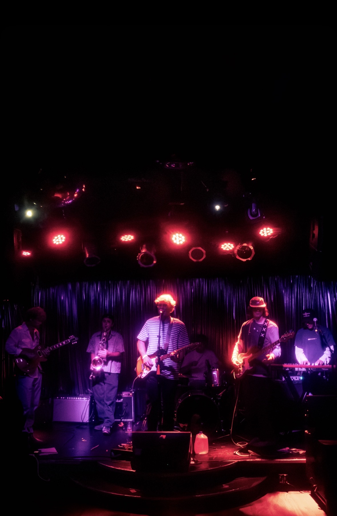 Six-piece band on a club stage lit in red and purple